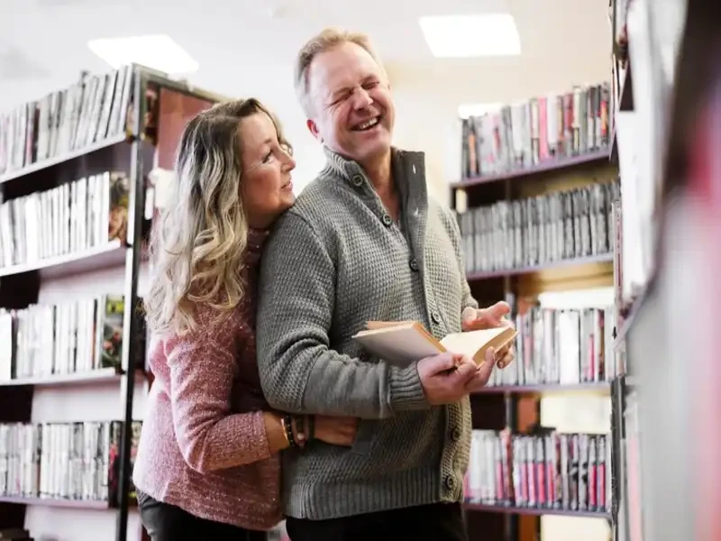 old couple enjoying exploring assorted novels and non-fiction titles stacked on shelves in a used book store setting